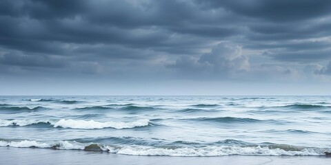 Fototapeta premium Gentle waves undulate against the shore as clouds gather in the darkening sky, seascapes, horizon line, beach scene