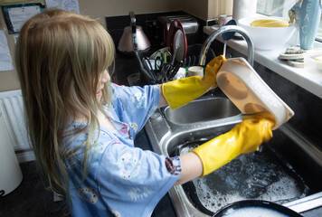 Child (8-9 years old) in Yellow marigold gloves washing up inside kitchen during day cleaning cat bowl