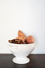 antique white ceramic bowl with chestnuts and sweet potatoes on white wall is wooden surface