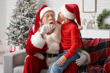 Shocked Santa Claus and cute little girl telling her wish on sofa in decorated room for Christmas