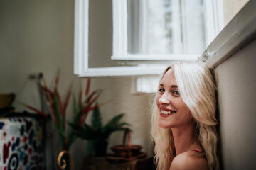 Smiling Blonde Woman Relaxing by an Open Window with Indoor Plants in the Background