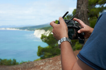 Landscape aerial photography. Man's hands with a remote control from a drone on the picturesque background of a sea bay. © ROMAN DZIUBALO