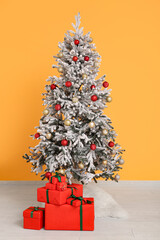 Beautiful decorated Christmas tree with gifts near orange wall