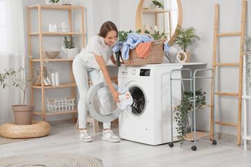 Young woman putting dirty clothes into washing machine at home
