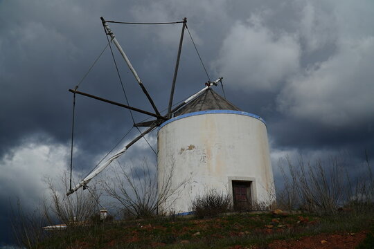 Traditional old Portuguese windmill on the N125 national road near the village of Budens, Algarve, Portugal. The mill under dark rain clouds, typical rough weather at the southwestern end of Europe.