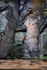 The beautiful, colourful and vibrant autumn foliage creates interesting patterns in the water created by a small waterfall, contrasting with the towering rock face. 