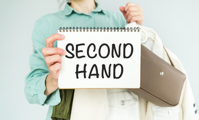 White plastic hangers, hand holding white paper . Text Second Hand. Trendy pastel white background. Forgetting fast fashion going eco-friendly.