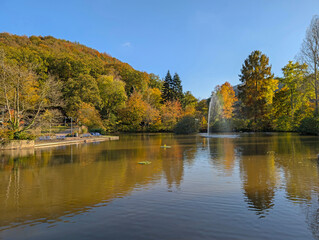 The spa garden in Annweiler with pond and water fountain at sunshine and autumnal trees