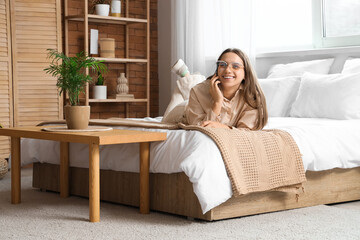 Obraz premium Pretty young woman talking by phone on bed in light bedroom