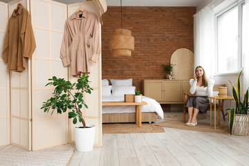 Pretty young woman talking by phone in stylish bedroom