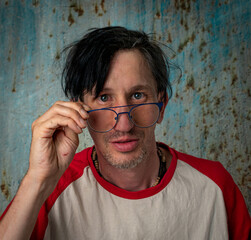 White man with black hair with glasses and white red tshirt near old wall