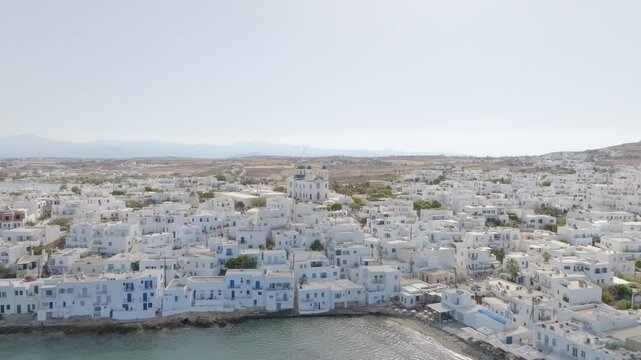 Aerial drone footage showcasing Naousa village on Paros island, Greece, moving forward over the Cycladic architecture and revealing the serene Aegean Sea.