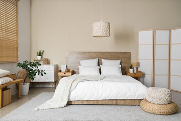 Comfortable bed, bedside tables, chest of drawers and folding screen in interior of bedroom