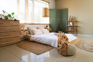Stylish interior of bedroom with comfortable bed, chest of drawers and folding screen