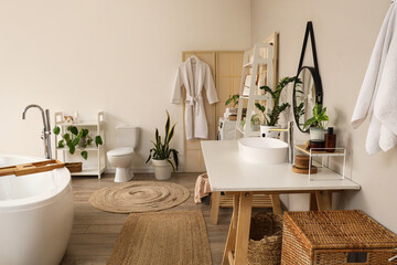 Bathtub, houseplants and table with modern sink in interior of bathroom