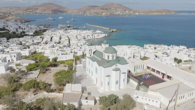 Aerial drone footage of Naousa village on Paros island, Greece, capturing the scenic view while moving upward, revealing the traditional Cycladic architecture and the Aegean Sea.