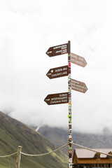 A directional signpost in the Georgian mountains during autumn, pointing to various hiking destinations under a cloudy daytime sky