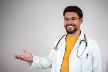 Doctor young man, medical professional holding something in empty hand isolated over grey background. 