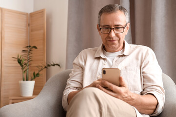 Old man with mobile phone sitting in armchair at home
