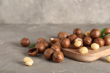 Wooden board with tasty macadamia nuts on grey background