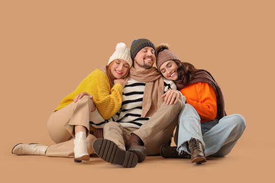 Man and two beautiful women in autumn clothes sitting on beige background. Polyamory concept