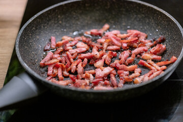 Frying small pieces of smoked bacon in frying pan.