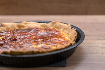 A quiche with fried smoked bacon and cheese in a pie pan on table.