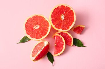 Cut fresh grapefruits and leaves on pink background