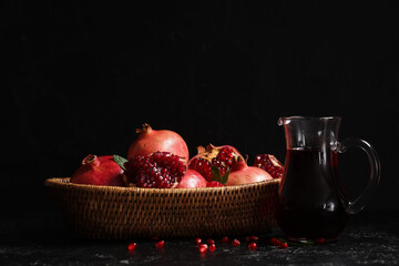 Jug of fresh pomegranate juice and wicker bowl with fruits on black background