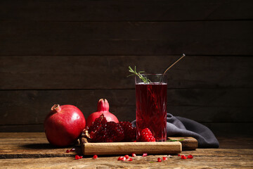 Glass of fresh pomegranate juice with rosemary and seeds on wooden background