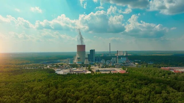 Aerial view of an industrial power plant surrounded by forests during a sunny day with clouds in the sky