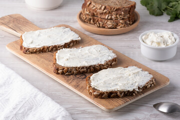 Slices of whole grain bread topped with cream cheese on a wooden cutting board in a cozy kitchen setting