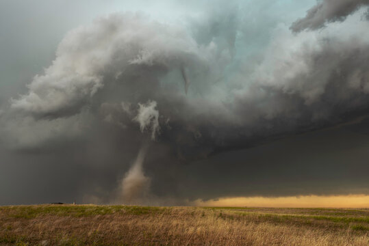 A thin, beautiful tornado spins across a dirt field in southeastern Wyoming during a Summer storm.