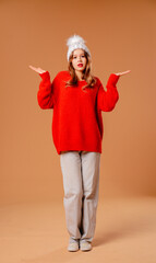 Young girl in red sweater and warm hat poses in studio on beige background