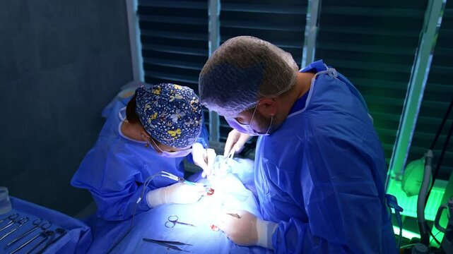 Bright light on the operational spot at thyroid surgery. Female surgeon and assisting doctor perform operation. Top view.