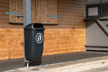 Black trash bin positioned near a wooden wall in a public area
