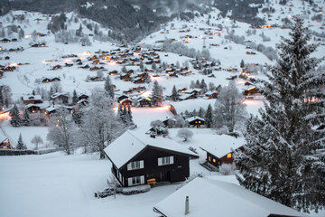 Grindelwald, under the soft glow of the night lights, transforms into a magical village where the snow glistens and each chalet seems to watch over the peaceful, slumbering mountains, Switzerland.