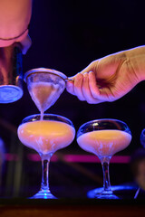 Bartender pours pink cocktail into martini glass with flair