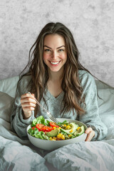 A smiling woman relishes a colorful, healthy salad while relaxing.