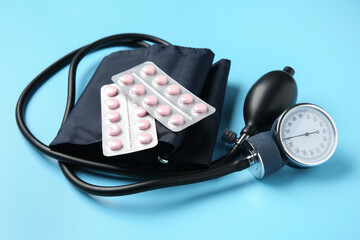 Blood pressure measuring device and pills on light blue background, closeup