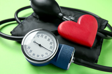 Blood pressure measuring device and heart figure on green background, closeup