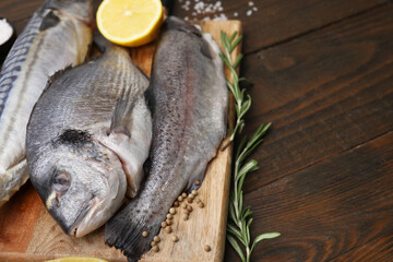 Sea food. Different types of raw fish, rosemary and lemon on wooden table, closeup. Space for text