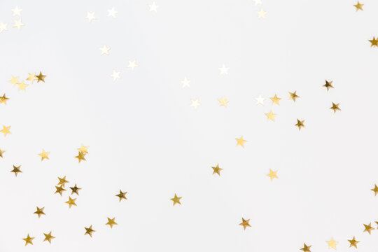 Gold sparkle confetti stars on a white background. Glitter, shine, bright. Christmas festive flat lay, winter holiday, new year, happy birthday concept. Banner for greeting card, top view, copy space.