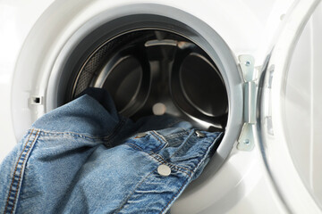 Washing machine with dirty denim jacket indoors, closeup