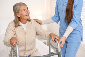 Fototapeta premium Nurse helping senior woman with walking frame in clinic