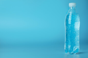 Plastic bottle of water on light blue background, space for text