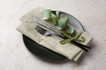 Black plate, cutlery, napkin and eucalyptus branch on gray textured table, closeup