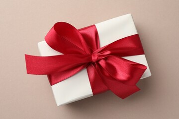 Gift box with red bow on beige background, top view