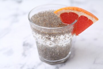 Glass of drink with chia seeds and grapefruit on white marble table, closeup