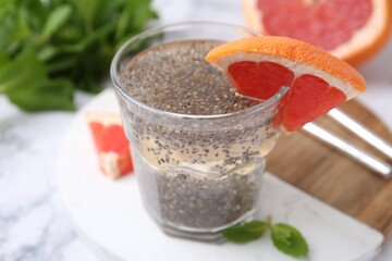 Glass of drink with chia seeds and grapefruit on white marble table, closeup